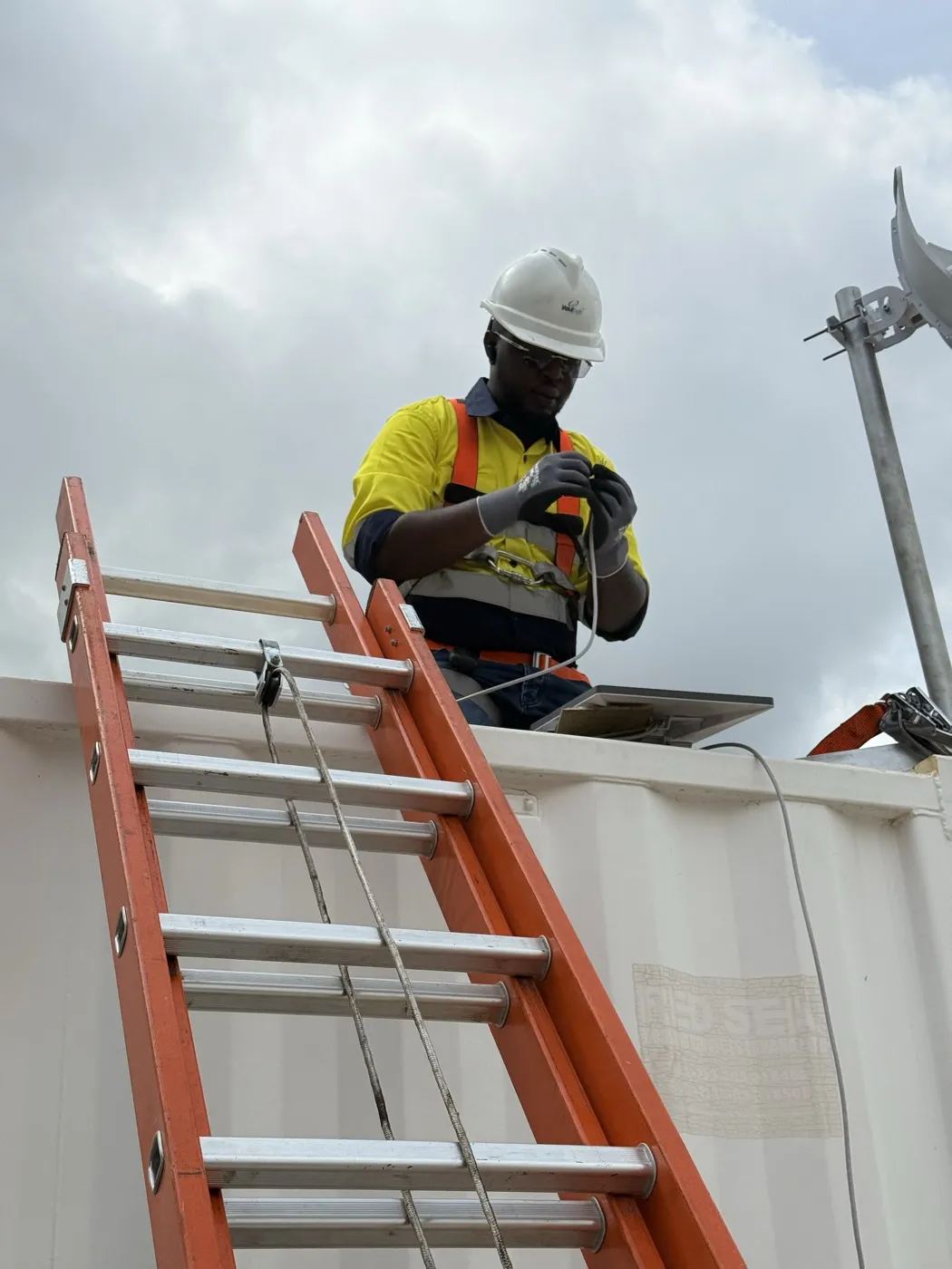 Kofi in a hard hat on site, wiring equipment on a container roof